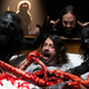 Dave Grohl sits in a pile of intestines, surrounded by zombies, as Studio 666 director does the devil horns behind him.